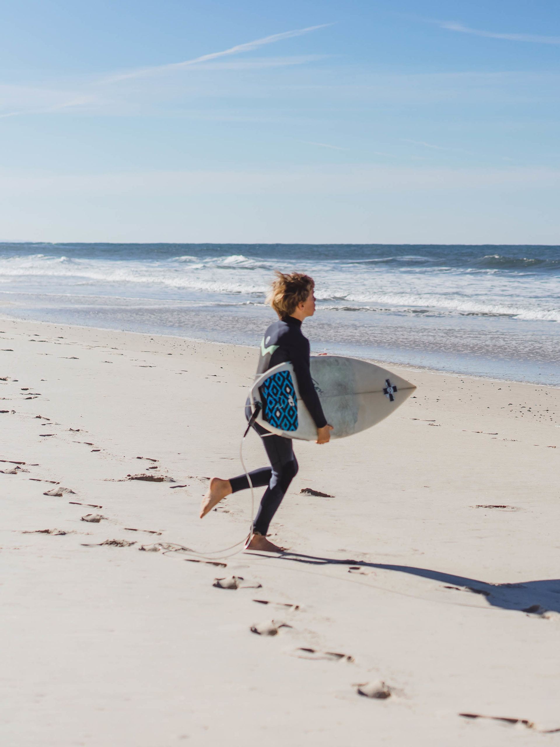 boy at the beach runs into the water with a surf board