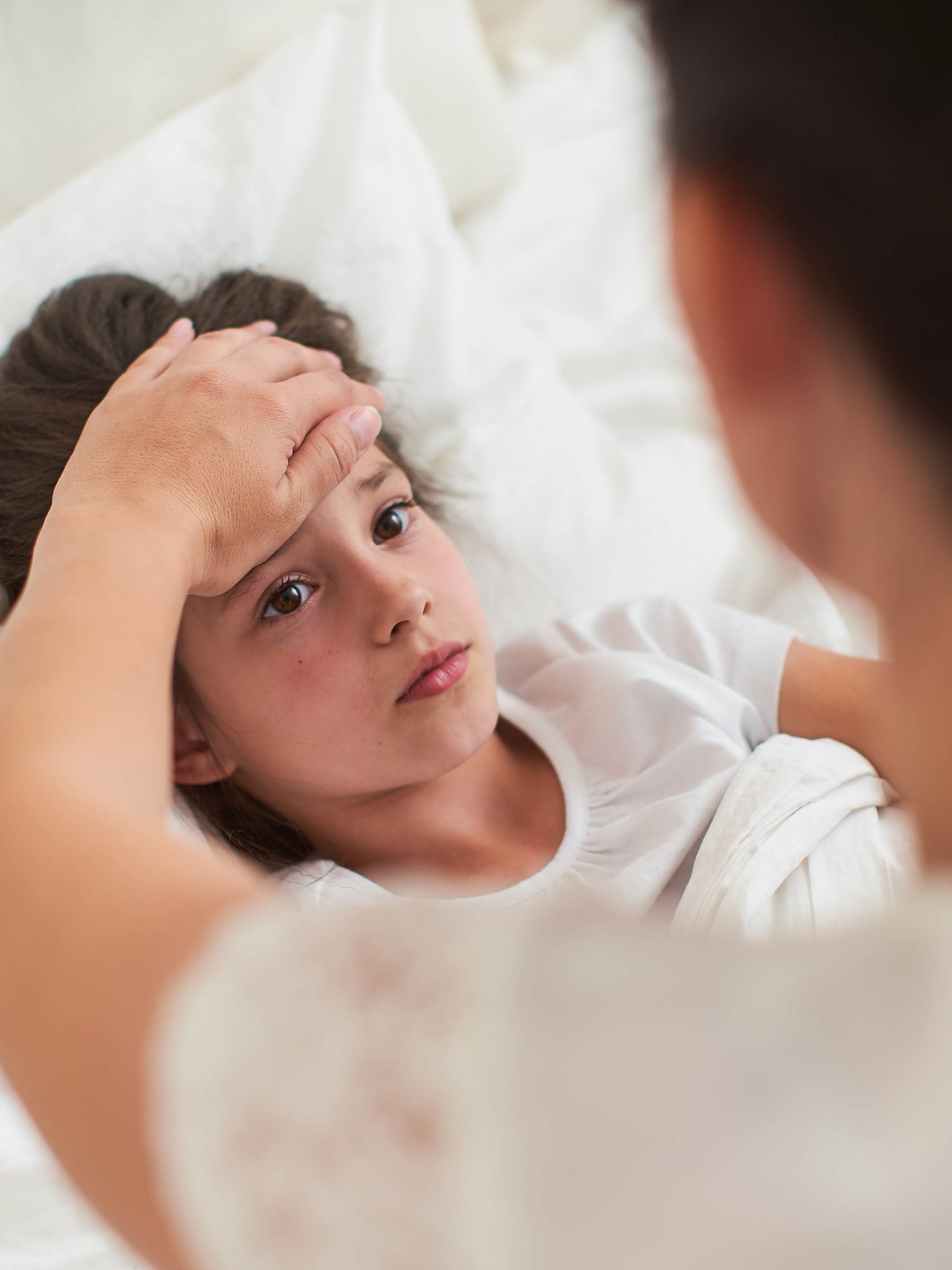 sick little girl lying in bed with fever while mom checks her temperature