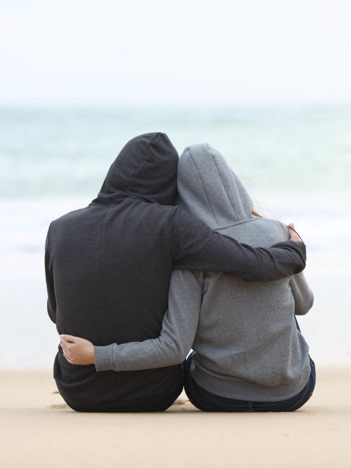 Father and daughter hugging sitting on the beach on a rainy day