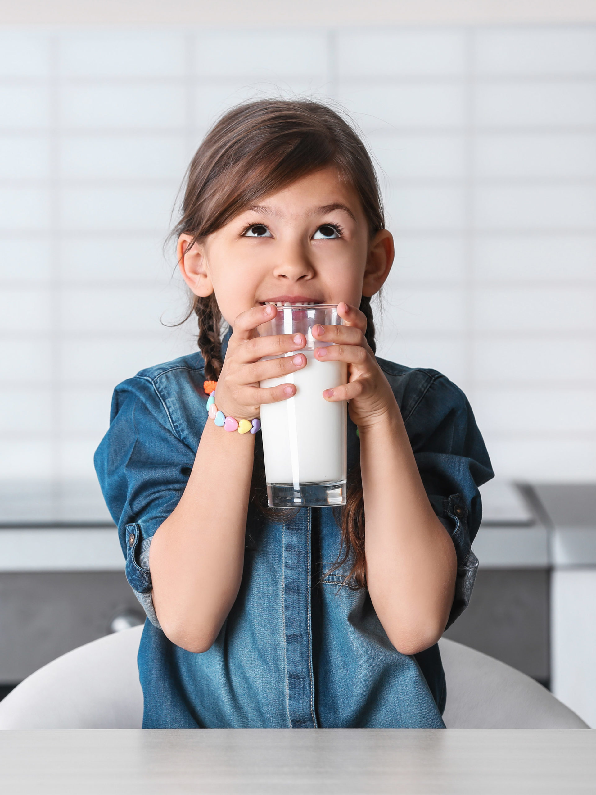 School aged little girl drinking milk at table in kitchen