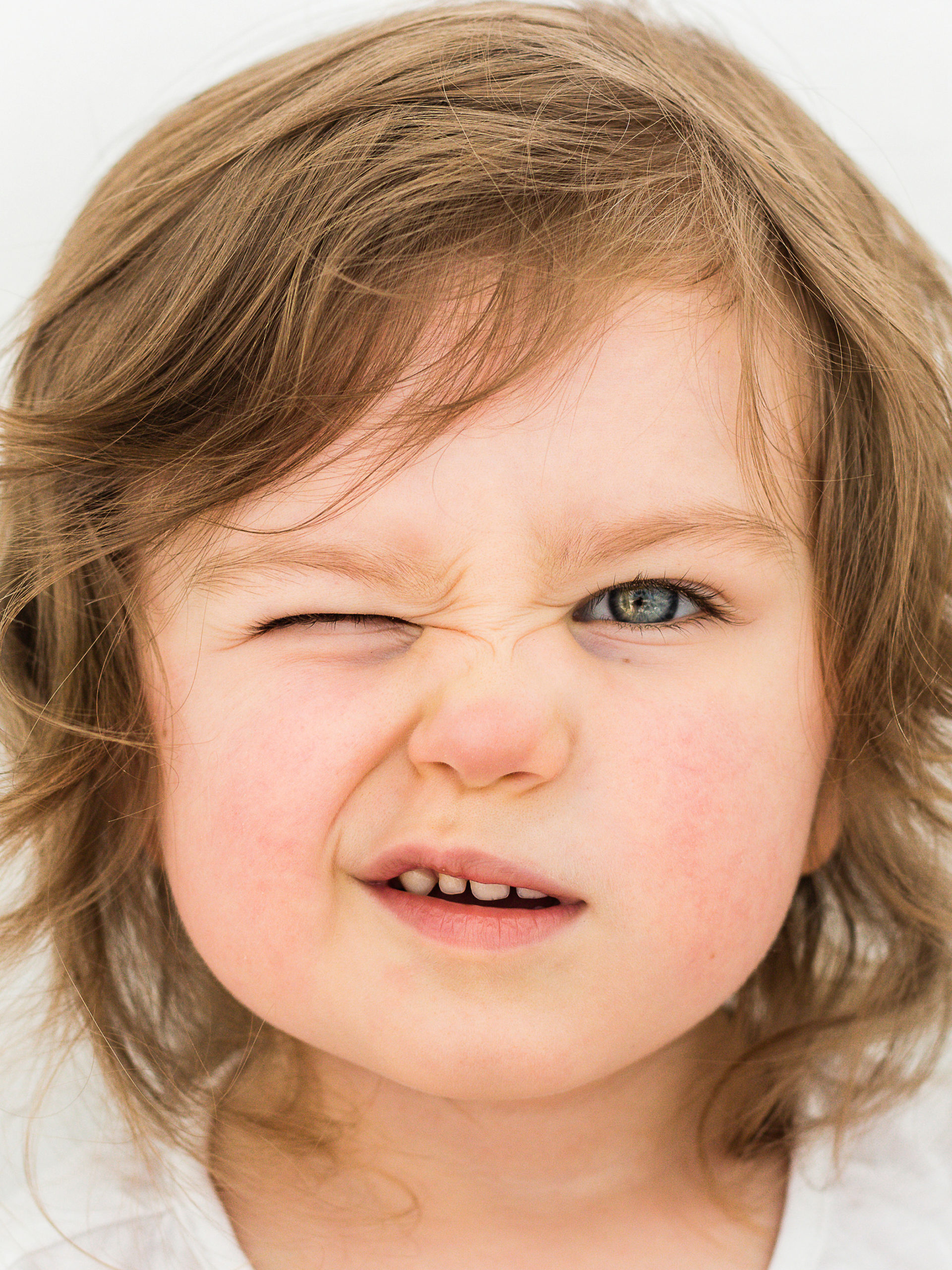 young girl with an eye twitch with one eye closed staring at the camera